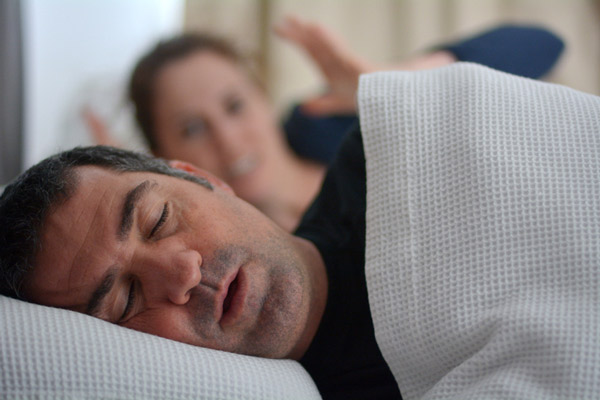 Man snoring in bed while woman covering her ears